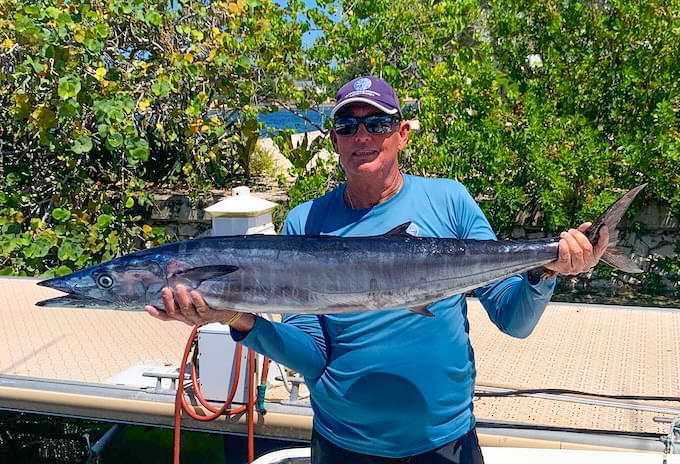 Angler smiling while holding a freshly caught wahoo during a trip with Grand Cayman fishing charters