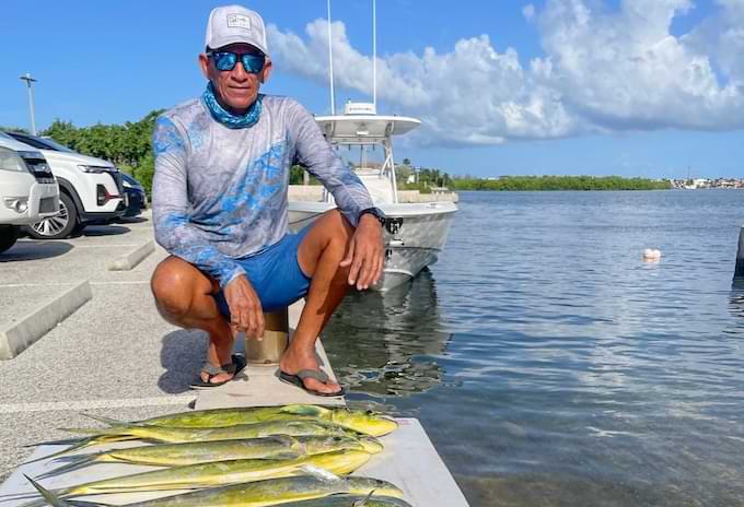 Angler kneeling beside a catch of four mahi mahi by the water after a trip