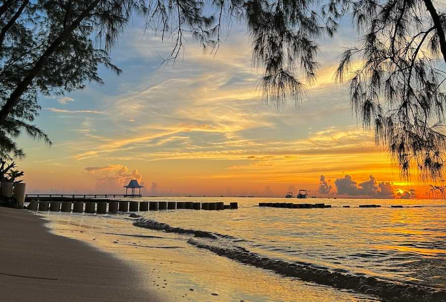 Calm evening at Rum Point with the sun setting over the horizon.