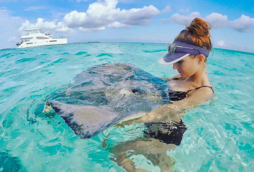 Woman holding a stingray while wading in the turquoise waters of Grand Cayman Stingray City