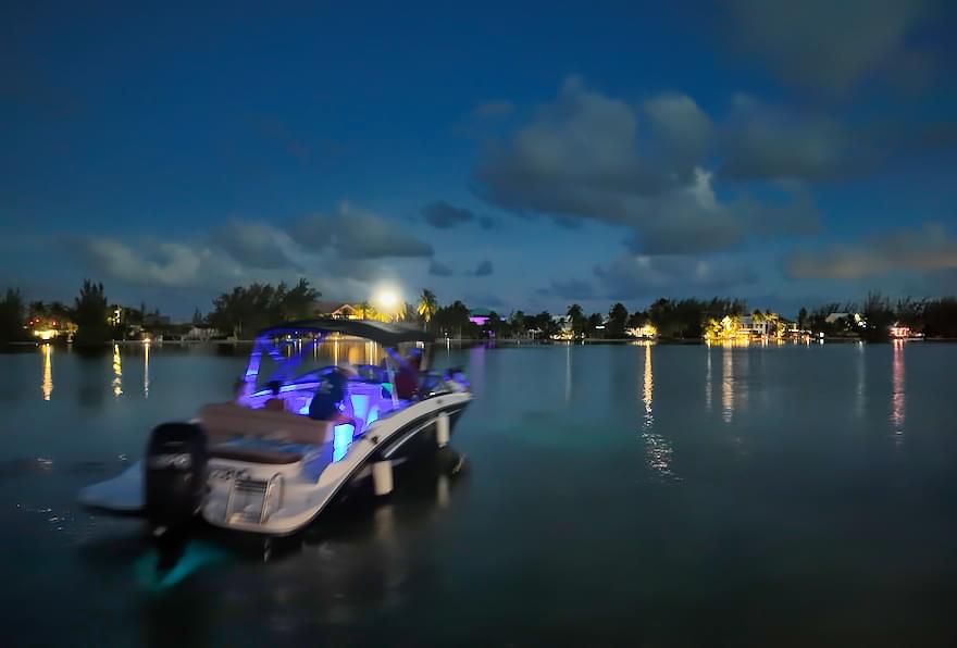 Boat is glowing with bioluminescence on the water under the night sky.