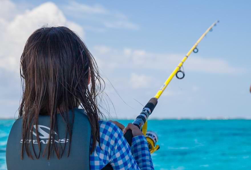 Girl fishing from a boat in the ocean, reeling in a catch during a trip fishing in Grand Cayman Islands.