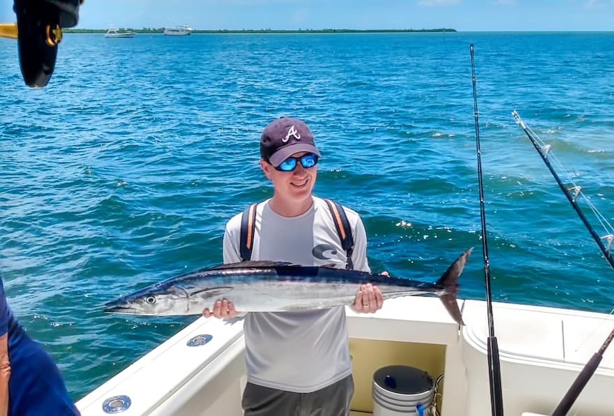 Man holding a Wahoo fish after a deep-sea fishing adventure in the Cayman Islands fishing.