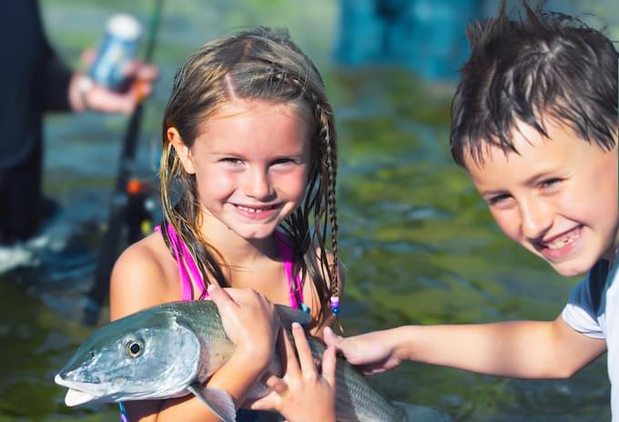 Two children holding a bonefish with excitement during a family fishing trip.