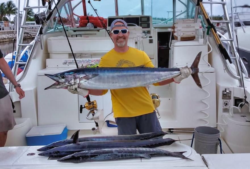Man holding a large wahoo fish on a boat after a successful Grand Cayman fishing charter