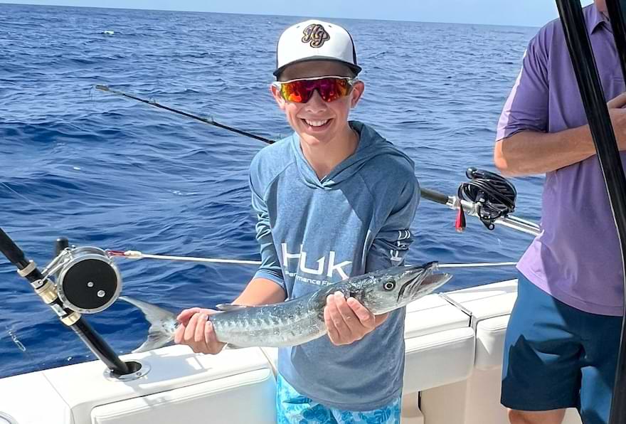 Young angler proudly holding a small barracuda on a boat with Cayman Islands fishing charters