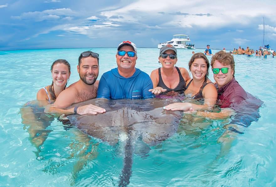 Group of tourists holding a stingray while wading in the shallow waters of a Cayman Islands fishing charter