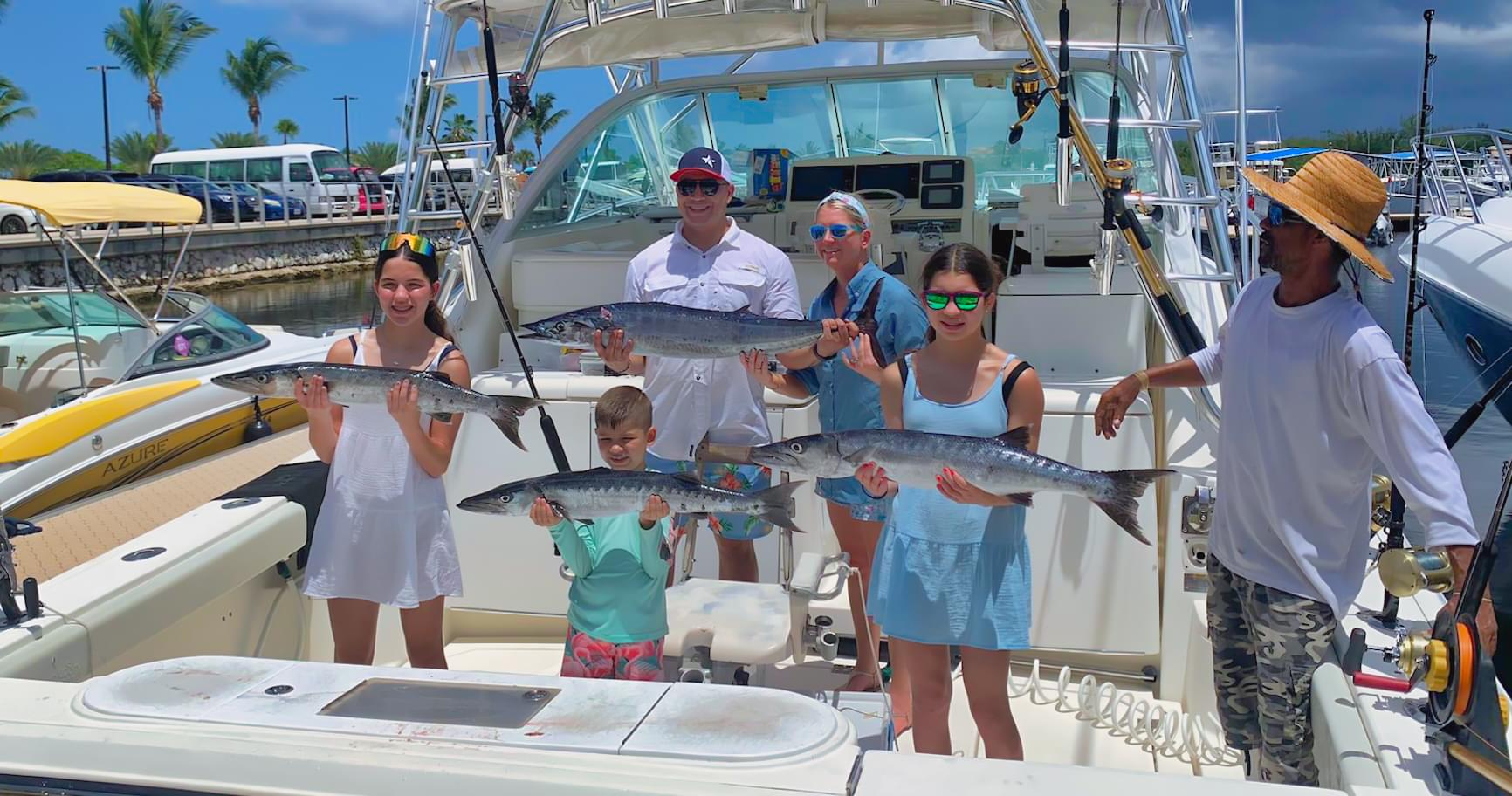 Family of anglers proudly holding their catch of barracuda after a Cayman Islands fishing charter trip