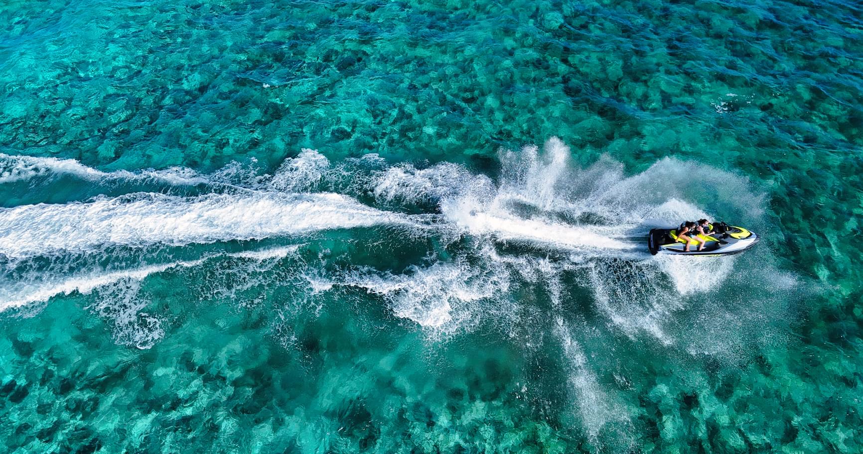 Aerial view of a jet ski Grand Cayman speeding across the turquoise waters of Grand Cayman, creating white wake trails.