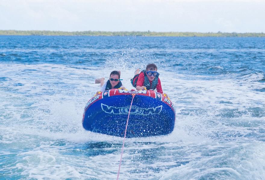 Two kids on a large inflatable tube are being pulled behind a boat, enjoying watersports in the Cayman Islands.