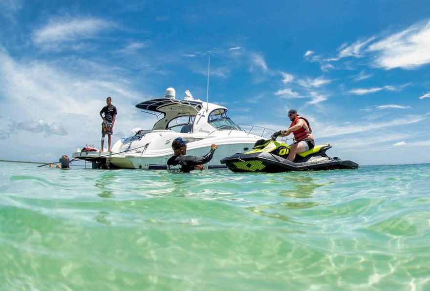 Person on a jet ski excursion in Grand Cayman parked next to a yacht in the shallow waters of the Cayman Islands.