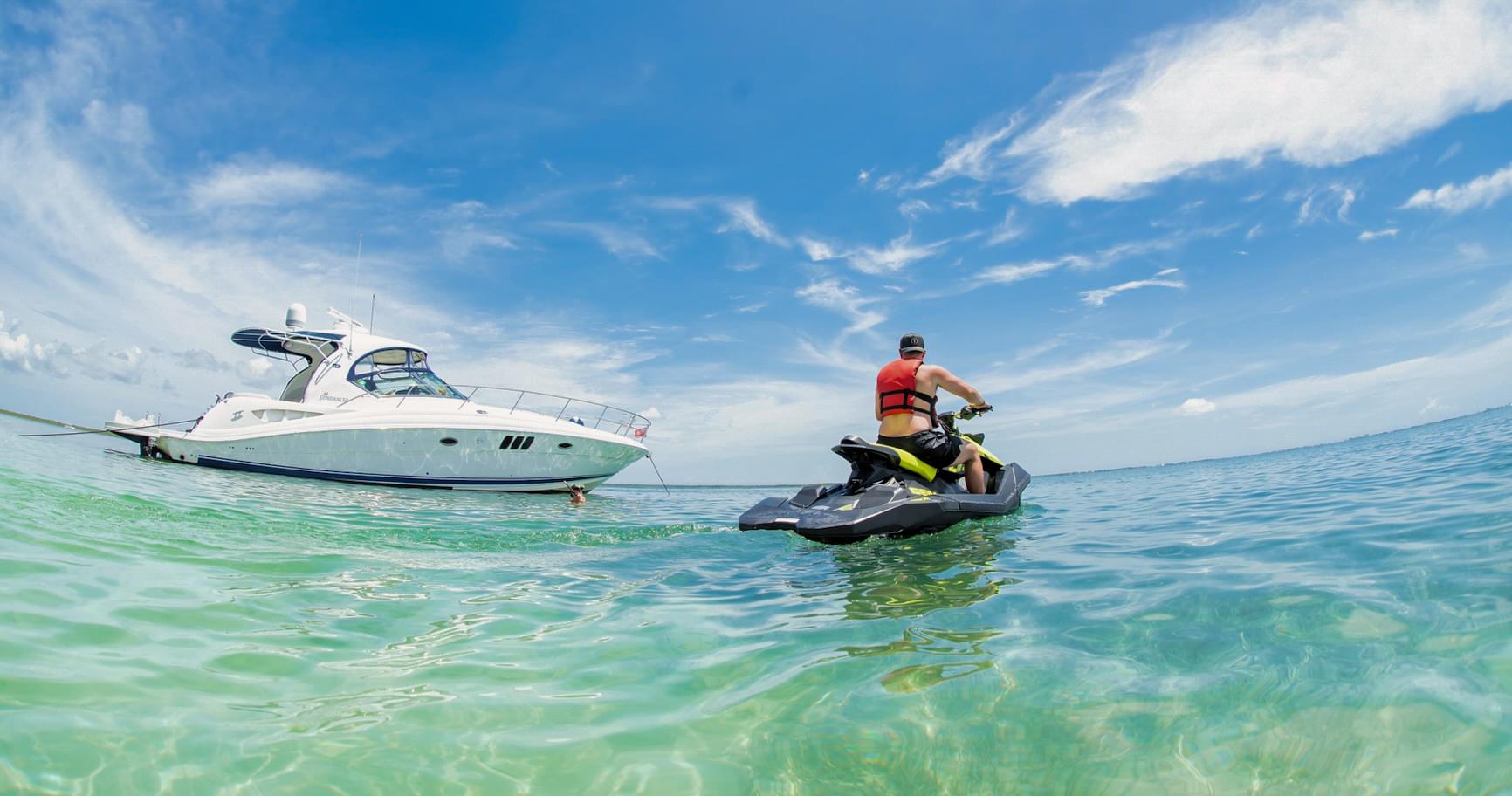 Grand Cayman jet ski rental approaching a luxury yacht, both anchored in the clear, shallow waters of the Cayman Islands.