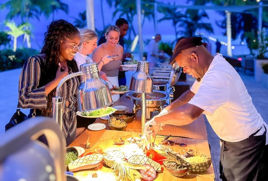 Guests enjoying a BBQ buffet at Rum Point Beach under twinkling lights in Grand Cayman