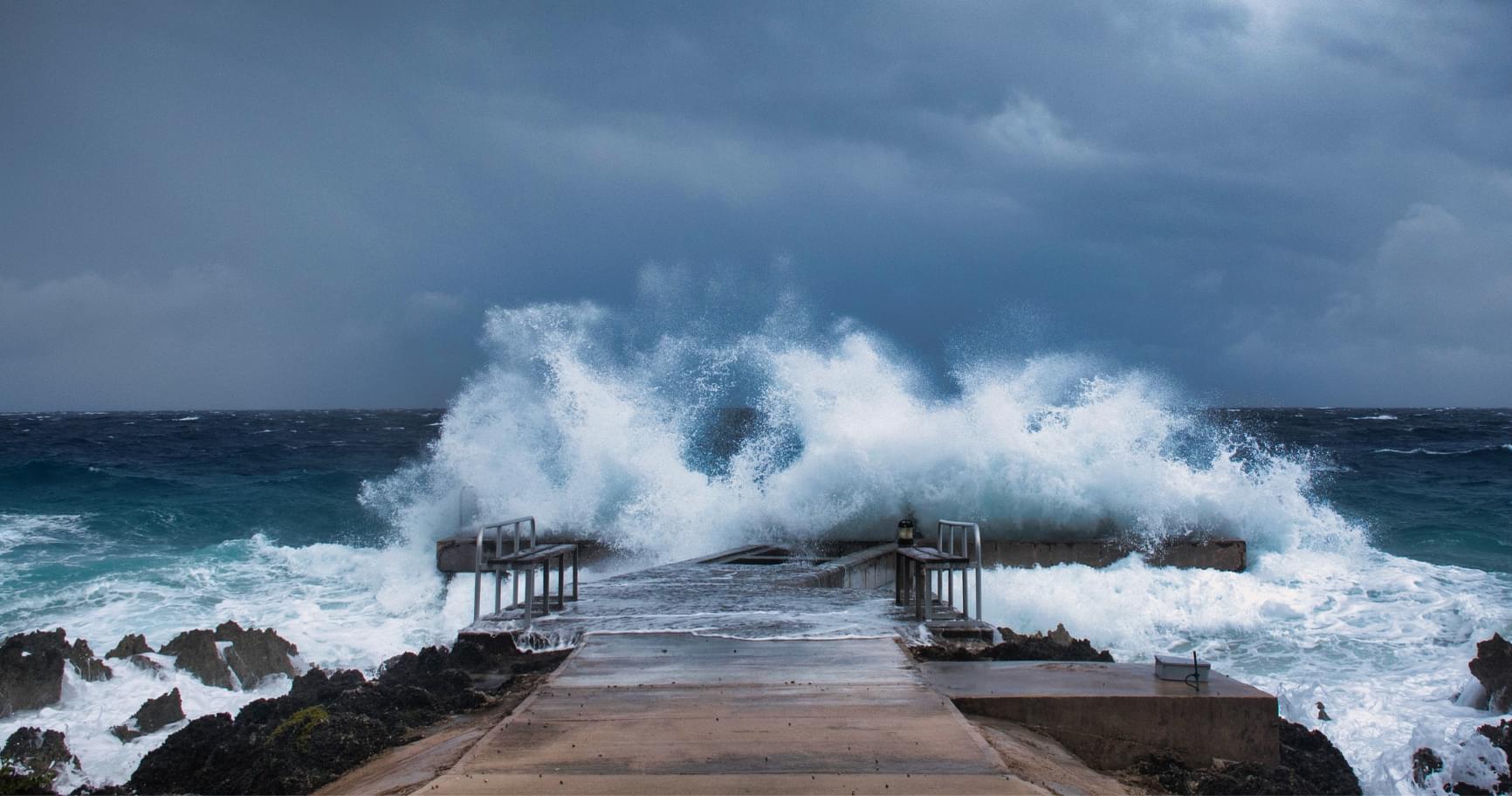 Waves crashing onto a pier, representing Cayman Islands hurricane history