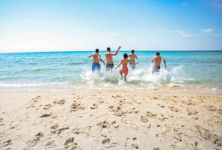 Friends running along the beach under sunny skies, enjoying the warm weather