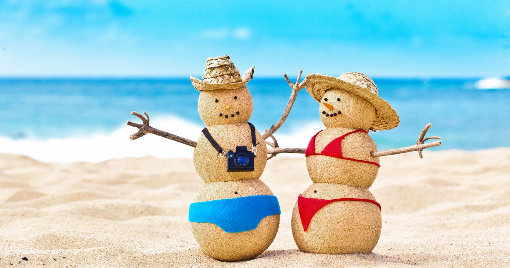 Sand snowmen on a beach symbolize holiday fun during Grand Cayman weather monthly