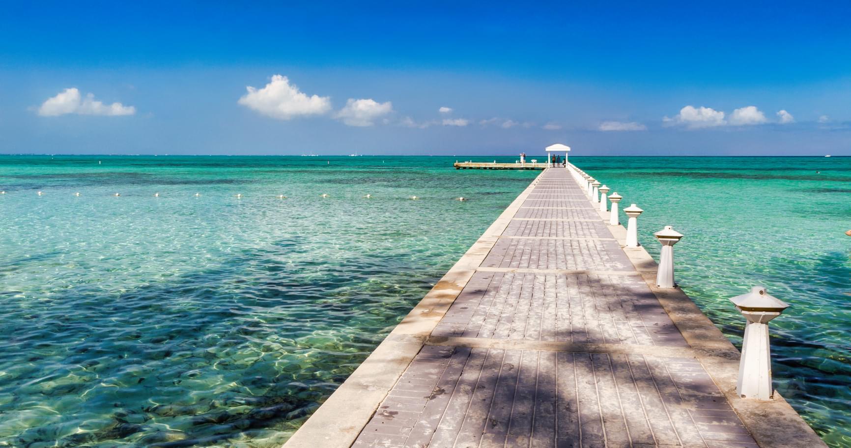 A wooden pier extends into crystal-clear waters, inviting visitors to enjoy the Grand Cayman water temperature