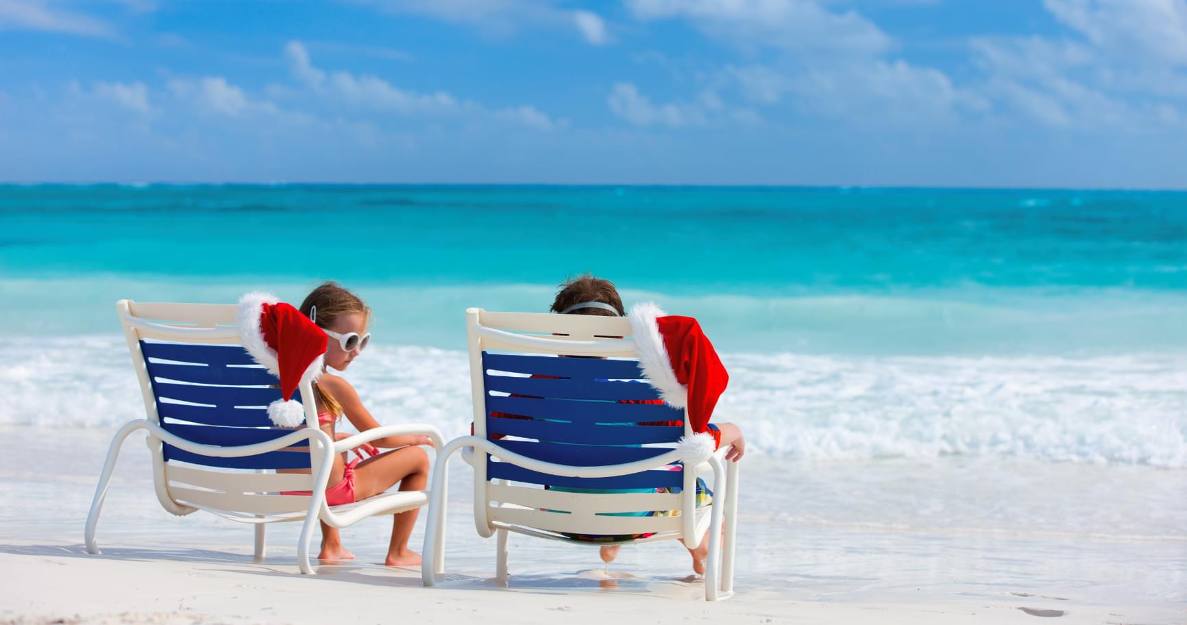 Kids relaxing on lounge chairs on Seven Mile Beach under sunny skies