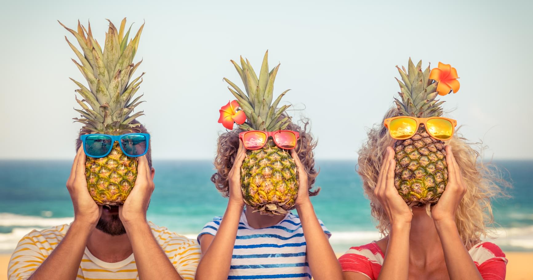 People are holding pineapples on the beach, enjoying tropical vibes