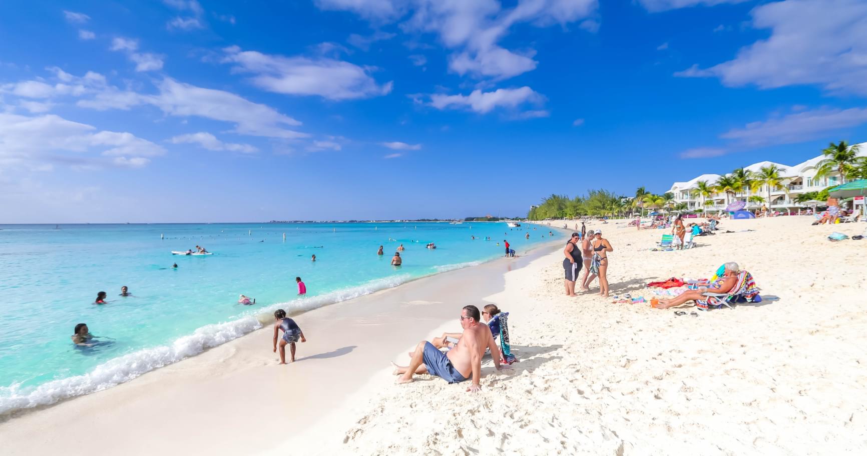 Families lounging on Seven Mile Beach under clear skies, enjoying warm weather during the best time to visit the Cayman Islands