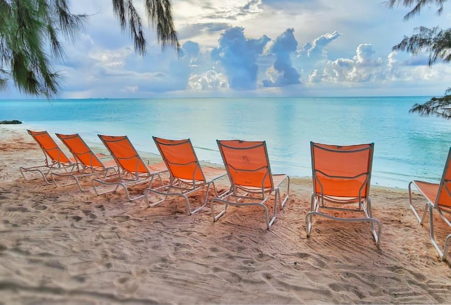 Vibrant orange lounge chairs on Rum Point Beach under clear skies offer a relaxing escape
