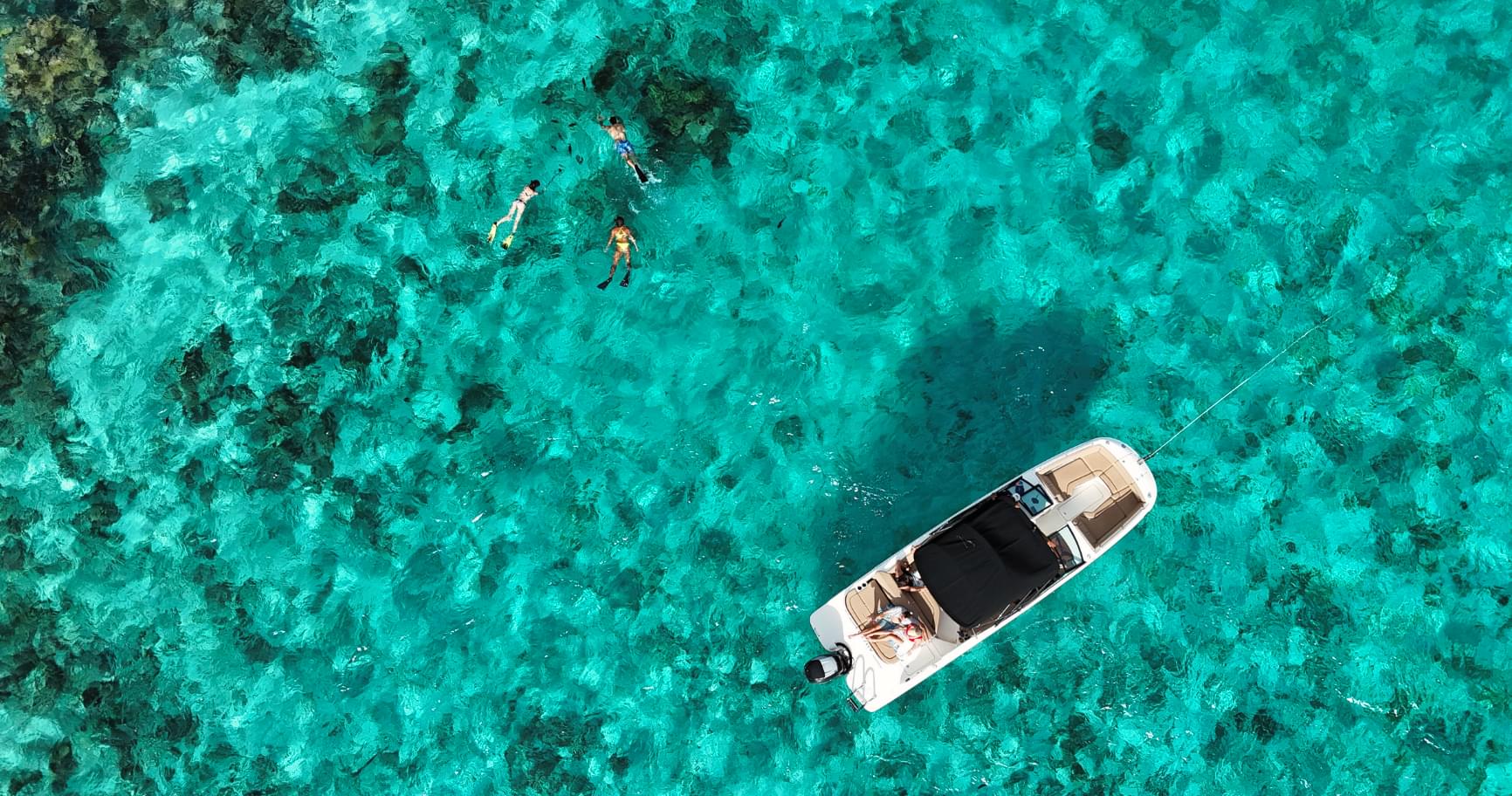 An aerial shot of a small boat surrounded by vibrant coral reefs showcases the island’s natural beauty