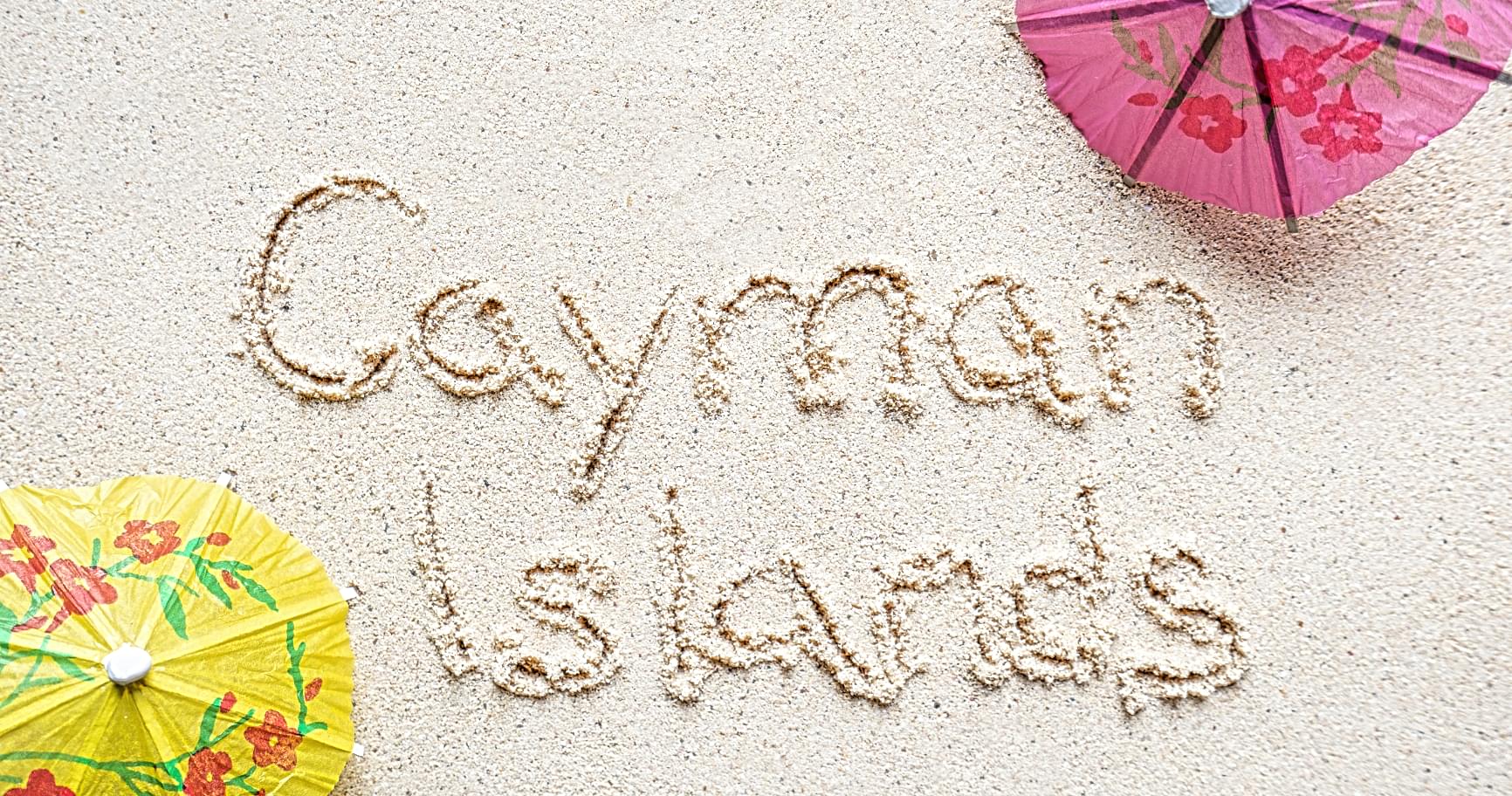 The Cayman Islands are written in the sand with vibrant parasols, capturing the island’s tropical charm