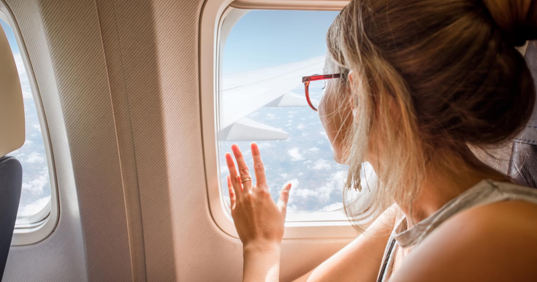 A woman gazing out of an airplane window, excited for her journey on direct flights to Grand Cayman