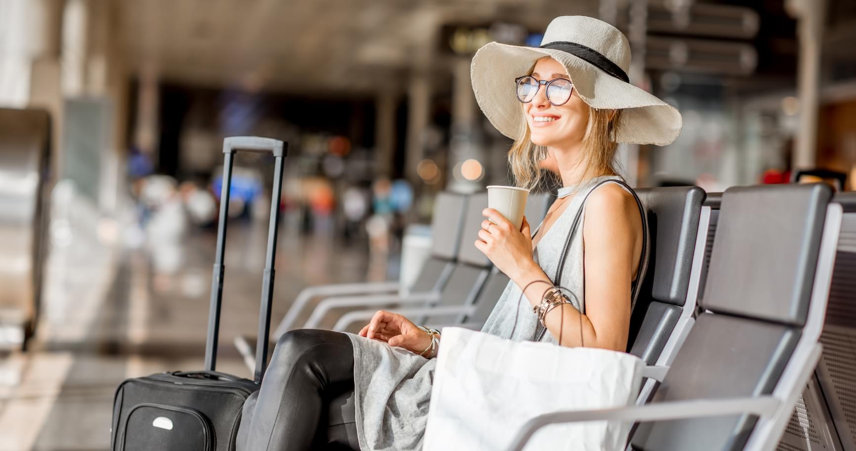A stylish traveler with luggage is sitting at the airport gate, waiting for a flight at affordable Cayman Islands flight prices