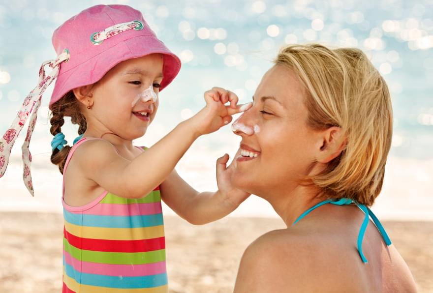 Kids apply sunscreen to mother at the beach after arriving in Grand Cayman and are excited about their vacation