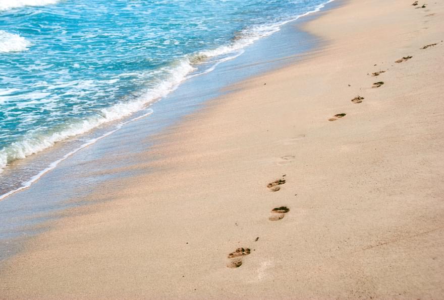 Footprints in the sand along a serene Grand Cayman beach encourage visitors to explore getting around Grand Cayman without a car