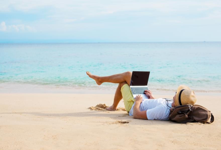 A man working on a laptop at the beach, showcasing digital nomad opportunities in the Cayman Islands