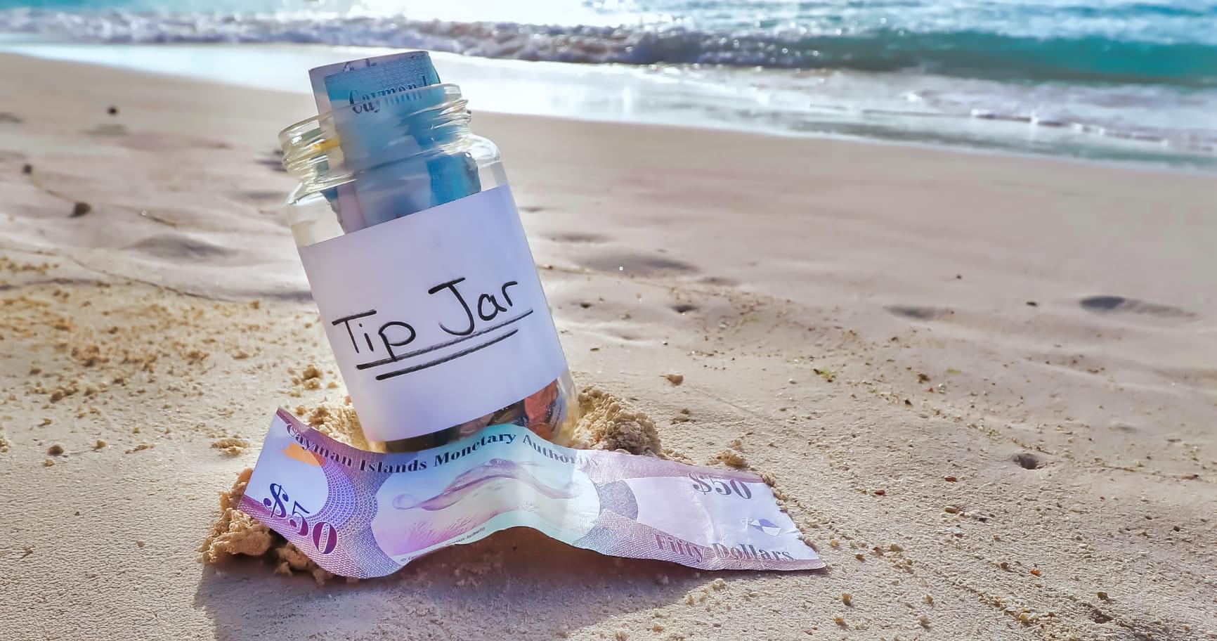 Stacked Cayman Islands dollars on the beach symbolizing tipping with everything from Cayman money to US dollars