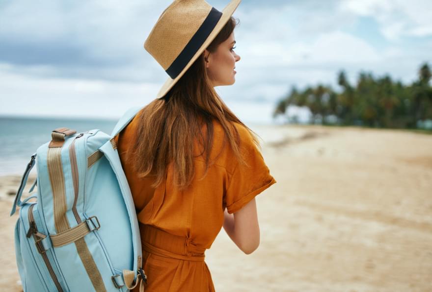 A woman with a backpack walking on the beach, reflecting on a peaceful destination for solo travelers
