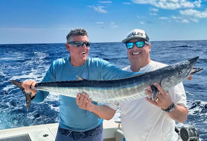 Two anglers proudly holding a freshly caught wahoo during a fishing trip in Grand Cayman.