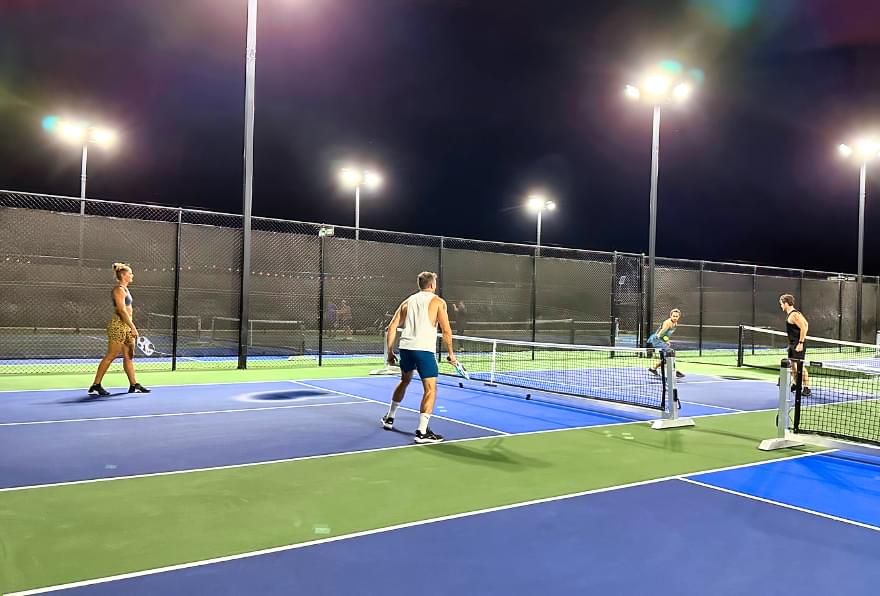 The group is playing pickleball on a well-lit court and enjoying an evening game in Grand Cayman.