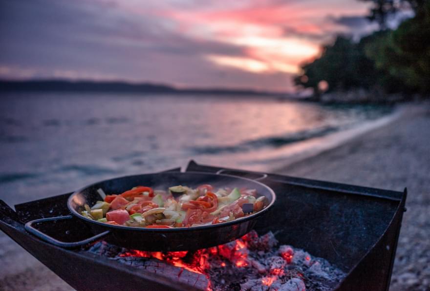 Outdoor paella cooking on a beach during sunset is a memorable addition to fun things to do in the Cayman Islands.