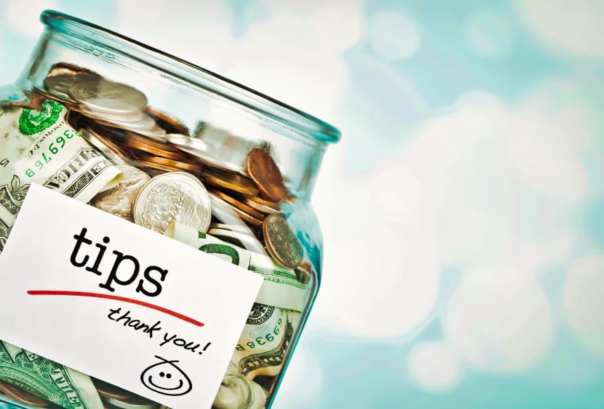 Tip jar filled with coins at a beachside establishment, highlighting tipping customs in Grand Cayman