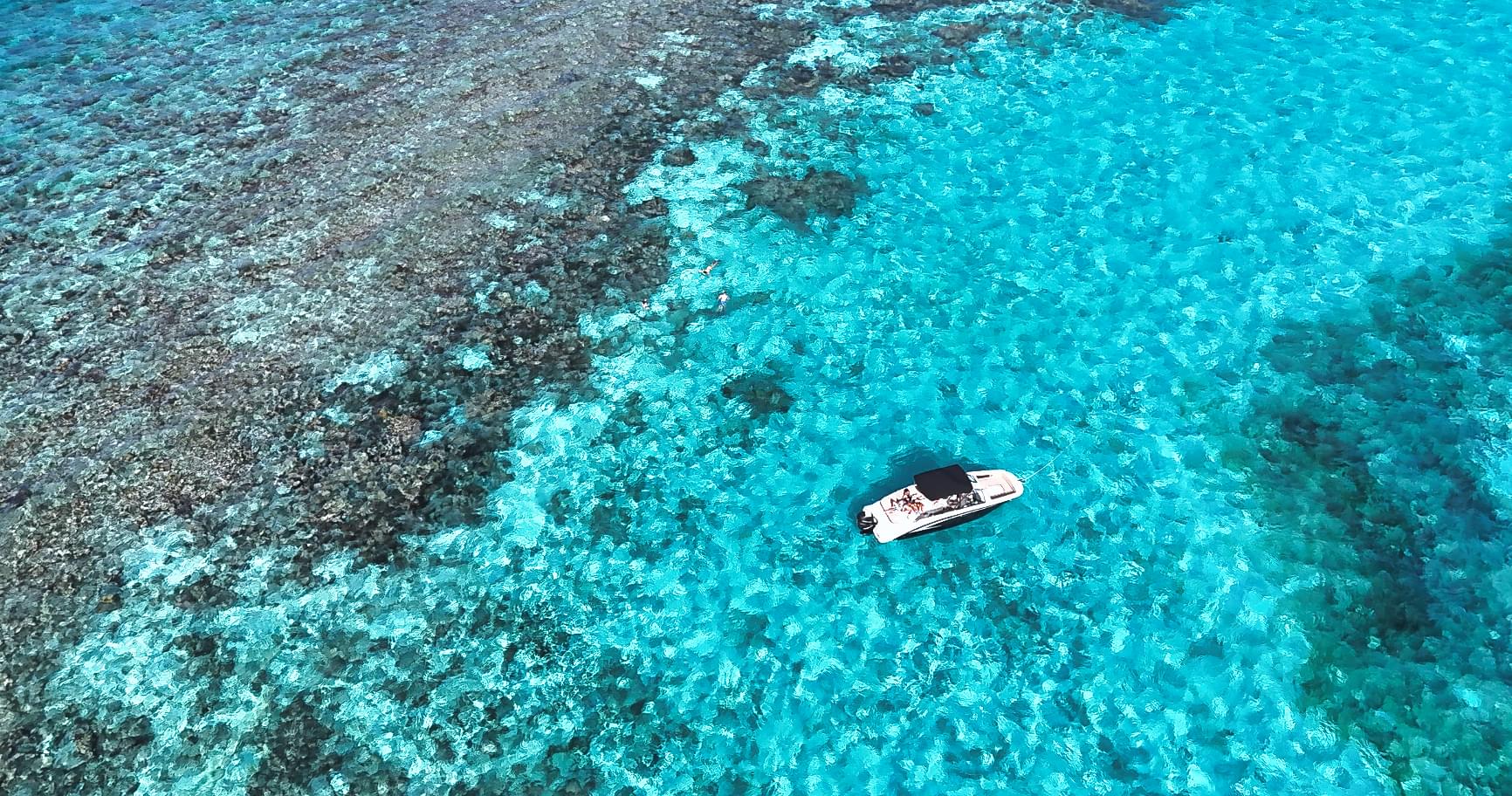 Aerial view of a boat over vibrant coral reefs, showcasing Grand Cayman boat tours