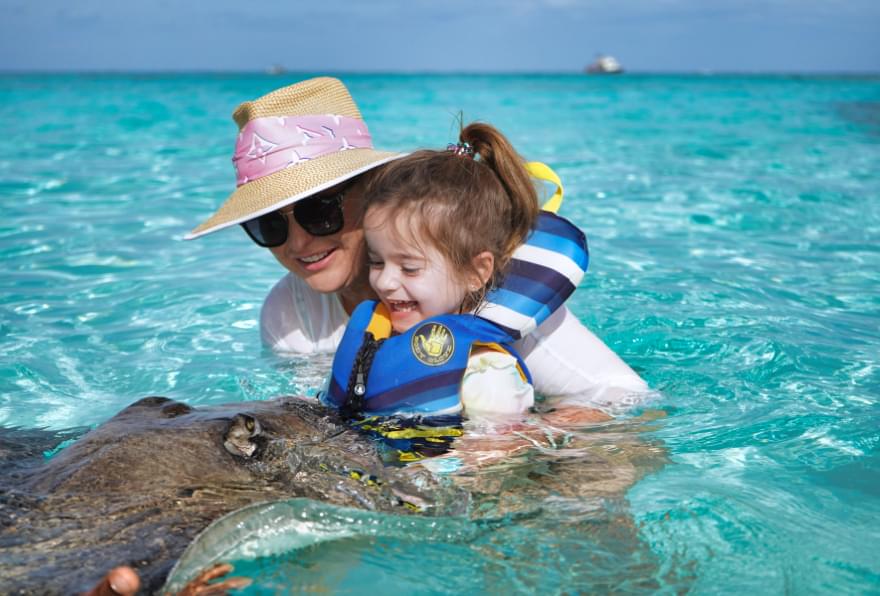 Mother and child interacting with a stingray during a Cayman Islands stingray city boat charter