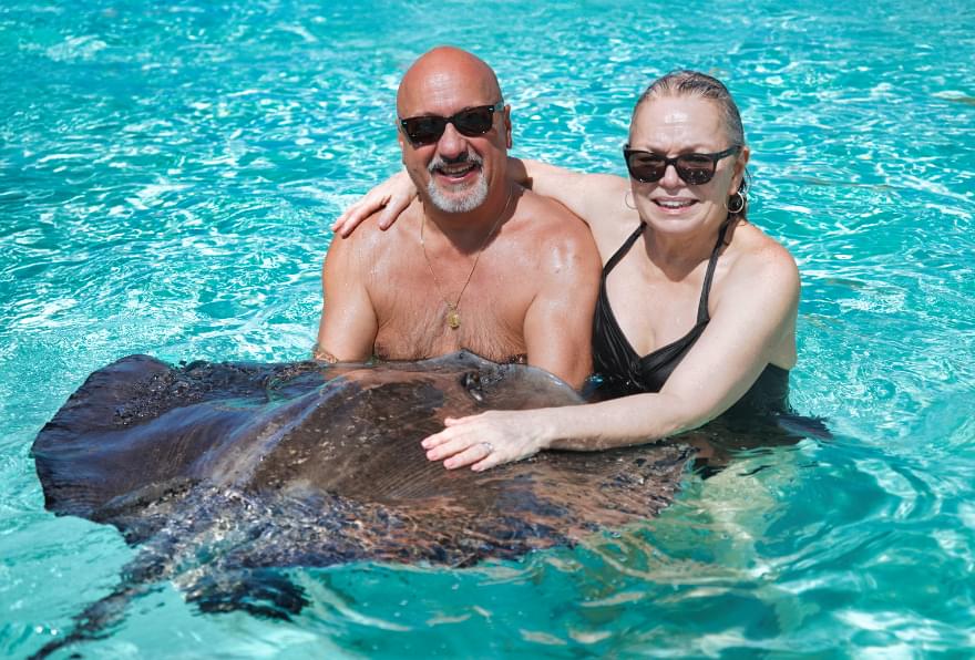 Couple interacting with stingrays at Stingray City, part of a private yacht charter in Cayman