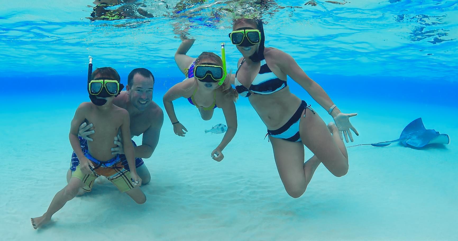 Family snorkeling together in calm, clear waters of Grand Cayman, enjoying Grand Cayman tourist attractions