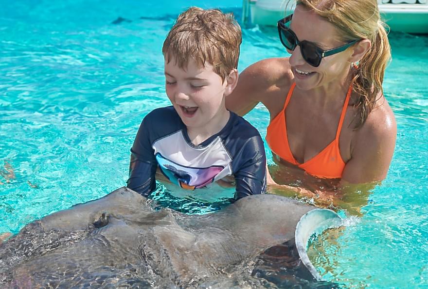 Mother and child interacting with stingray at Stingray City showcasing how it is safe to swim with stingrays