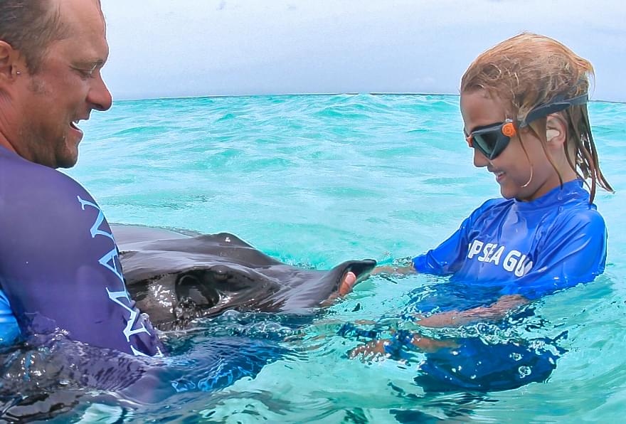 Young girl gently touching stingray guided by a tour operator emphasizing the family-friendly experience at Stingray City