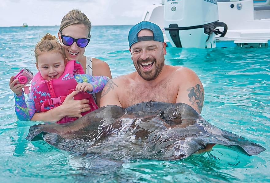Family smiling while holding a stingray at Stingray City creating unforgettable memories in calm waters, answering are stingrays safe to swim with