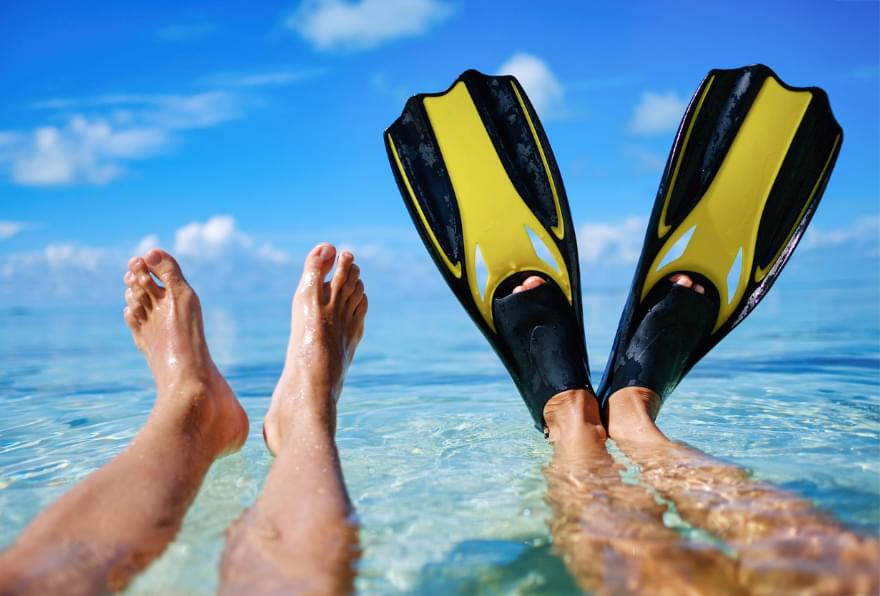 Feet with fins resting in shallow water symbolizing relaxation after a safe snorkeling experience