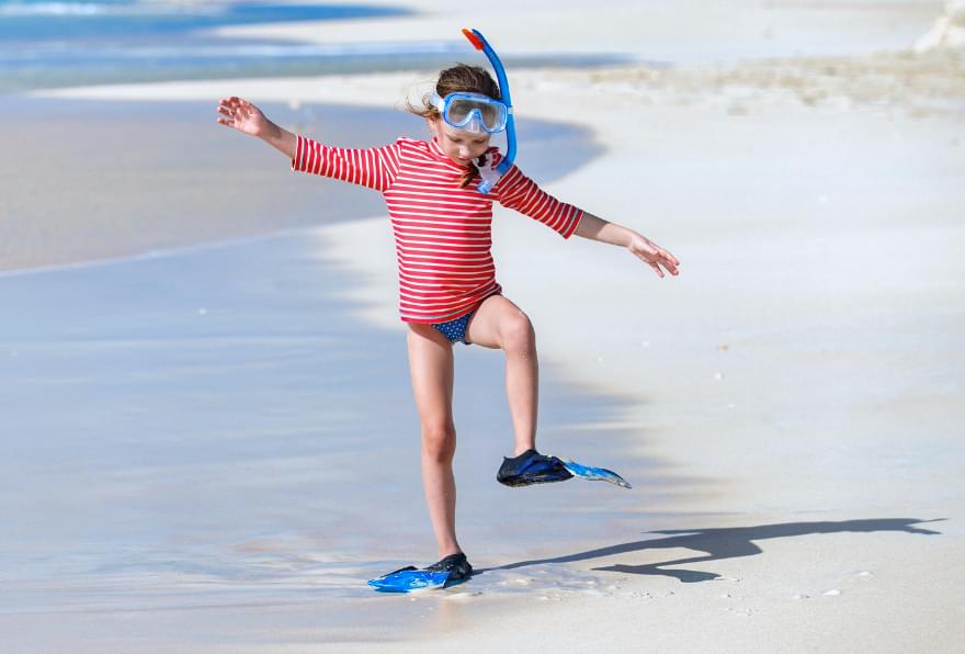 Child on the beach wearing snorkeling gear emphasizing safety for kids while snorkeling