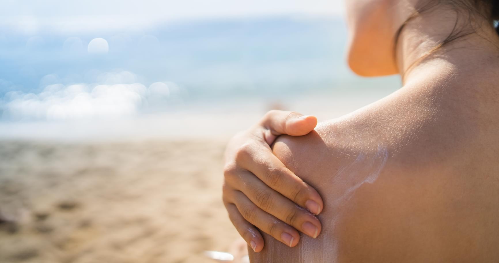 Person applying reef safe sunscreen on their shoulder at the beach to protect coral reefs