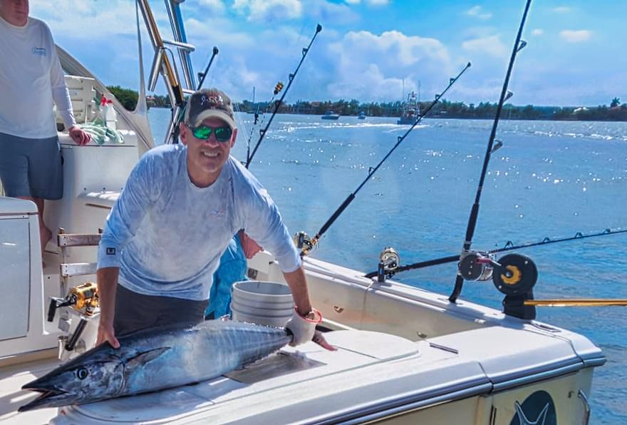 angler holding large wahoo aboard boat after deep sea fishing charters grand cayman