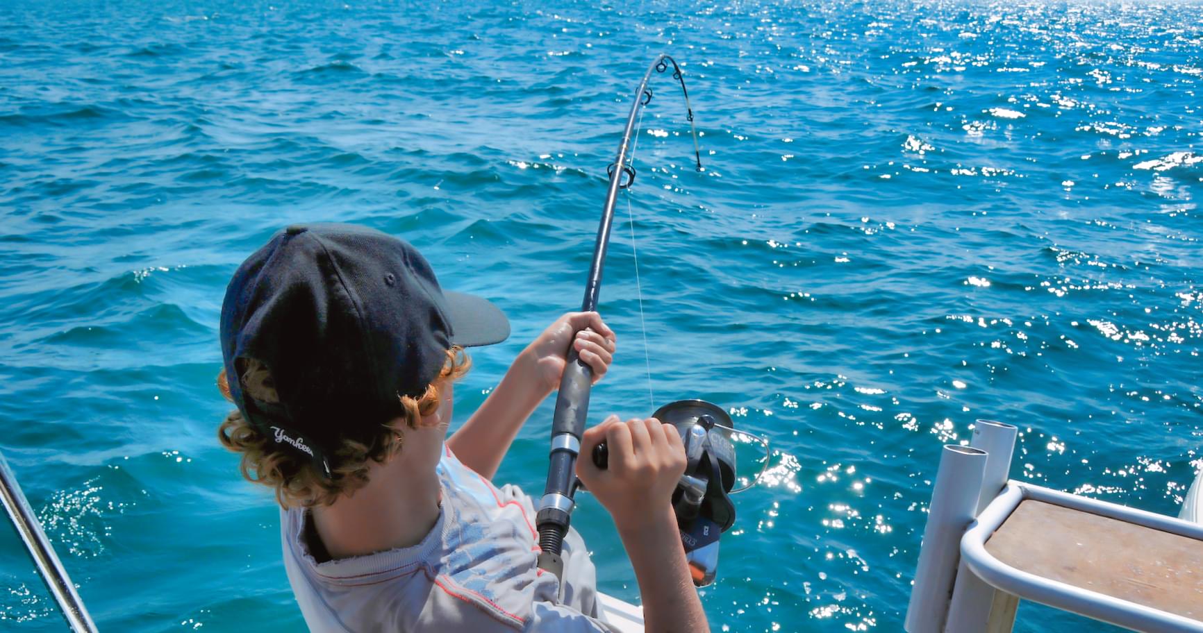 young angler reeling in fish on a sunny day at sea